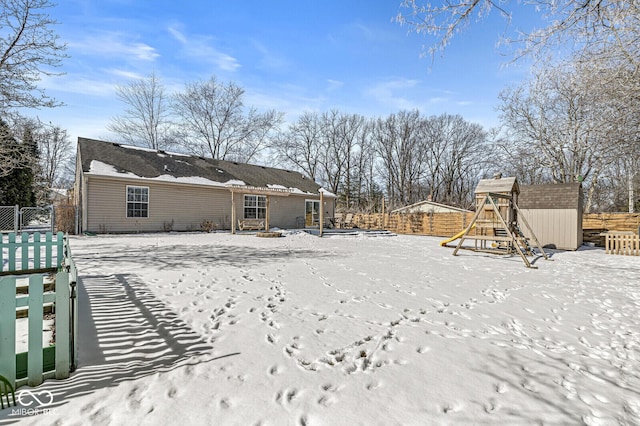 snow covered house featuring a fenced backyard and a playground