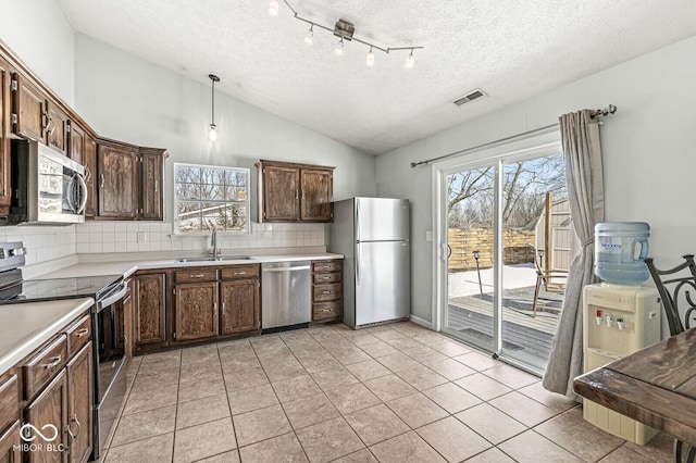 kitchen featuring lofted ceiling, stainless steel appliances, a sink, hanging light fixtures, and light countertops