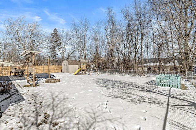 snowy yard with a fire pit, a storage unit, fence, an outdoor structure, and a playground