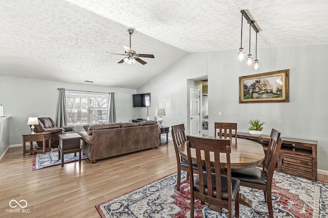 dining room featuring vaulted ceiling, a textured ceiling, light wood-type flooring, and a ceiling fan