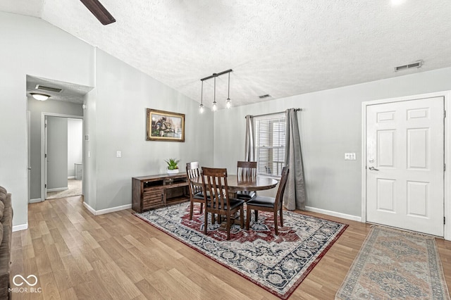 dining room with lofted ceiling, a textured ceiling, visible vents, baseboards, and light wood finished floors