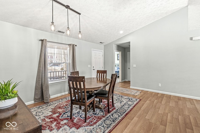 dining area with lofted ceiling, visible vents, a textured ceiling, light wood-type flooring, and baseboards