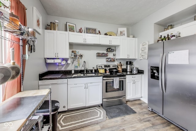 kitchen with white cabinets, appliances with stainless steel finishes, a textured ceiling, light wood-type flooring, and a sink