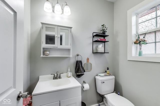 half bathroom featuring vanity, toilet, and an inviting chandelier