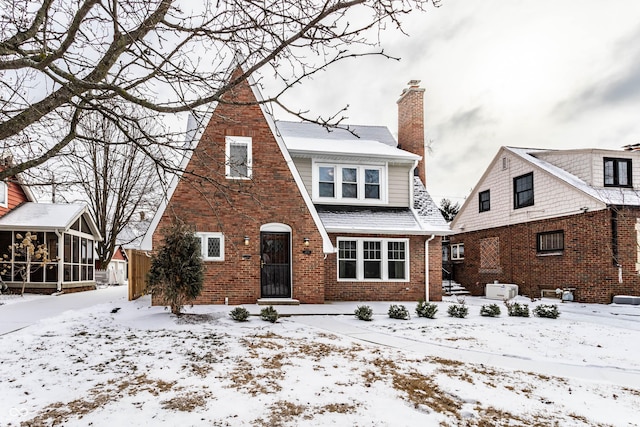 view of front of property with a sunroom, a shingled roof, a chimney, and brick siding