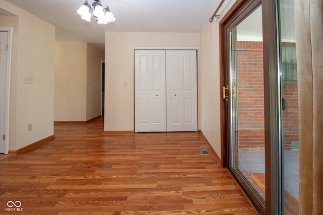 unfurnished bedroom featuring an inviting chandelier, light wood-style flooring, visible vents, and a closet