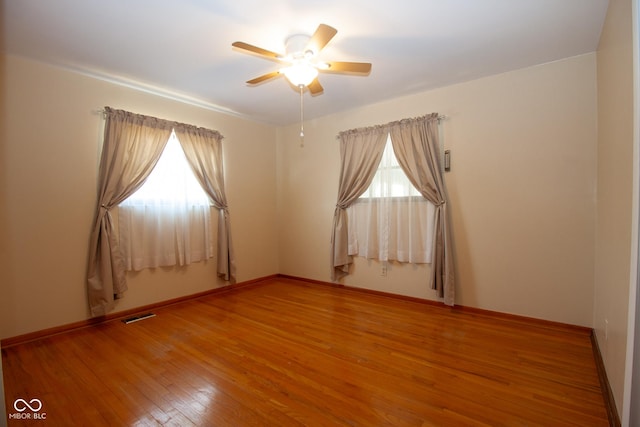 empty room featuring hardwood / wood-style floors, baseboards, visible vents, and ceiling fan