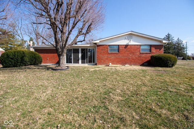 back of house with brick siding, a yard, and a sunroom