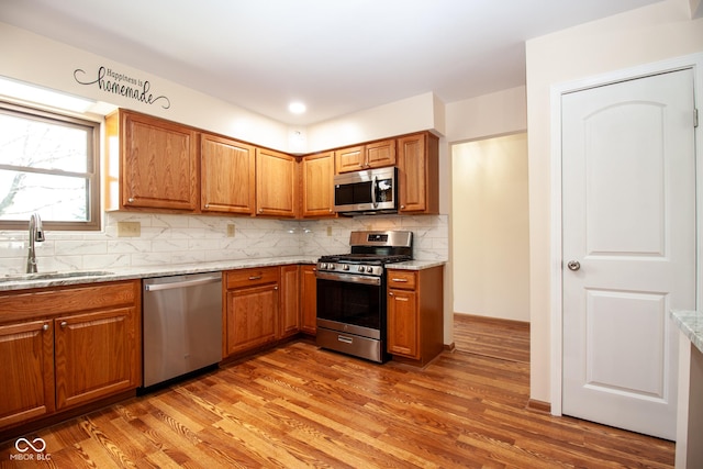 kitchen with light wood-style flooring, appliances with stainless steel finishes, brown cabinets, and a sink