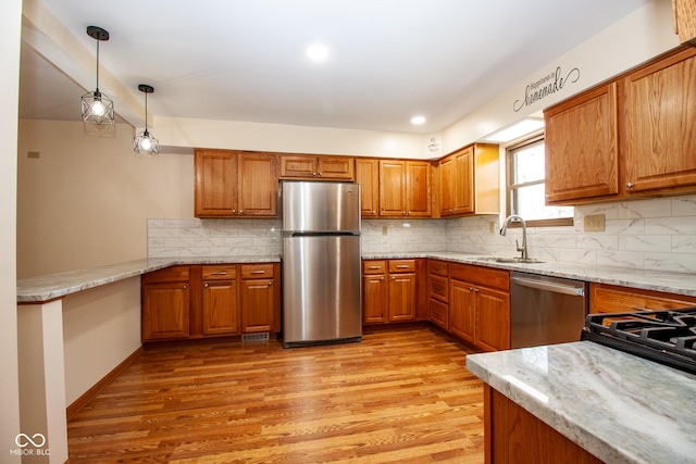 kitchen with brown cabinetry, appliances with stainless steel finishes, light wood-type flooring, and a sink