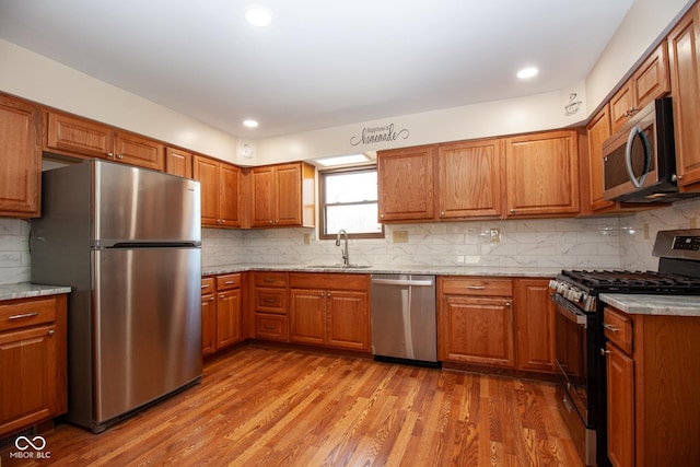 kitchen with wood finished floors, brown cabinetry, a sink, decorative backsplash, and appliances with stainless steel finishes