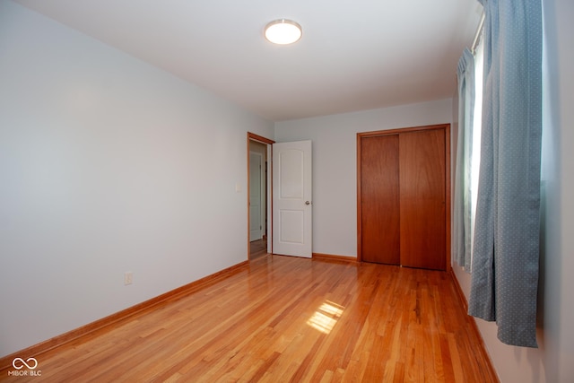 unfurnished bedroom with light wood-style flooring, baseboards, and a closet