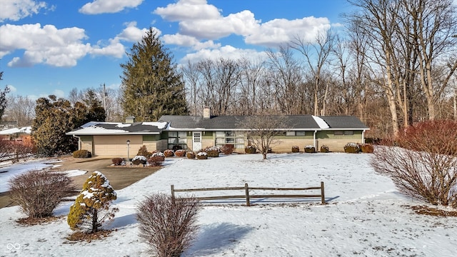 snow covered rear of property featuring a chimney, a fenced front yard, and an attached garage