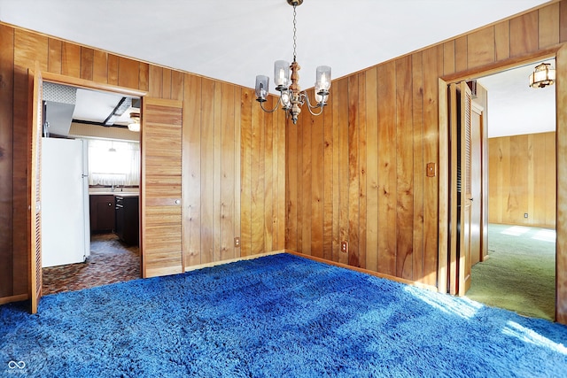 spare room featuring dark colored carpet, wood walls, a sink, and an inviting chandelier