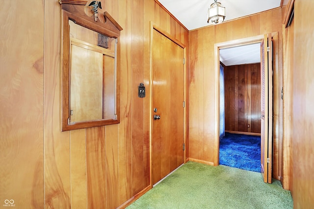 hallway featuring wood walls, carpet, and baseboards