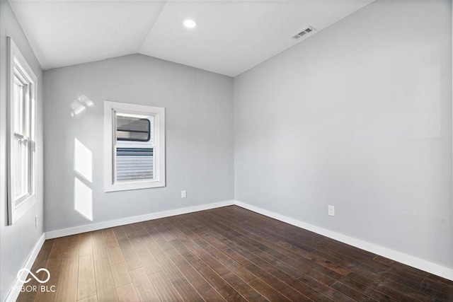 unfurnished room featuring visible vents, plenty of natural light, dark wood finished floors, and vaulted ceiling