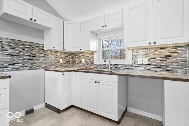 kitchen with decorative backsplash, lofted ceiling, white cabinets, and a sink