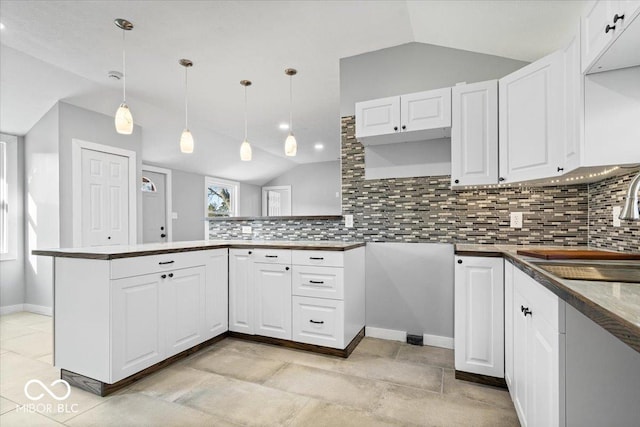 kitchen with lofted ceiling, a peninsula, a sink, white cabinetry, and backsplash