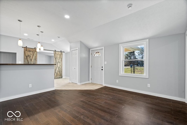 unfurnished living room featuring a barn door, wood finished floors, and vaulted ceiling