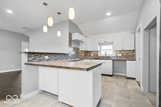 kitchen with a sink, a peninsula, white cabinets, and vaulted ceiling