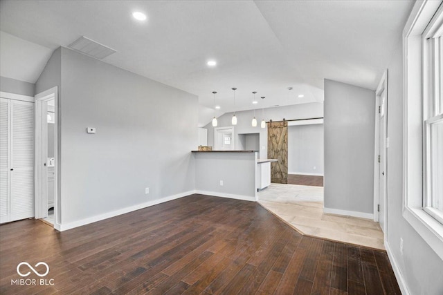 unfurnished living room featuring recessed lighting, hardwood / wood-style flooring, a barn door, and vaulted ceiling