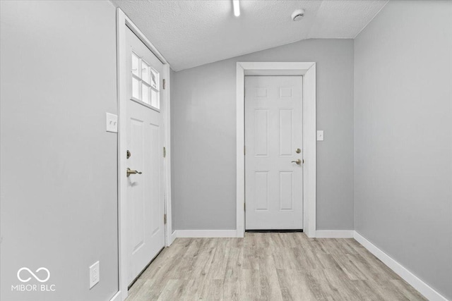 foyer entrance with vaulted ceiling, baseboards, light wood-type flooring, and a textured ceiling