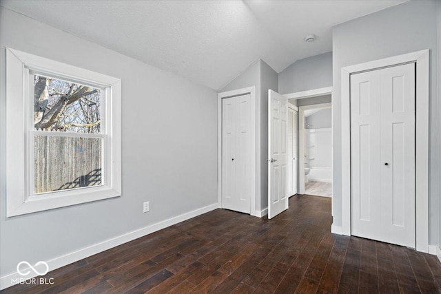 unfurnished bedroom with baseboards, lofted ceiling, and dark wood-style flooring