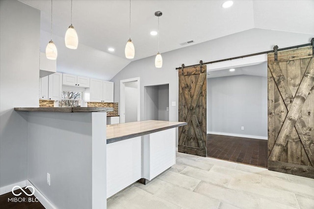 kitchen with visible vents, hanging light fixtures, vaulted ceiling, white cabinets, and a barn door