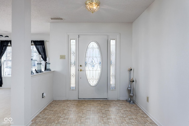 entrance foyer featuring a textured ceiling, baseboards, visible vents, and tile patterned floors