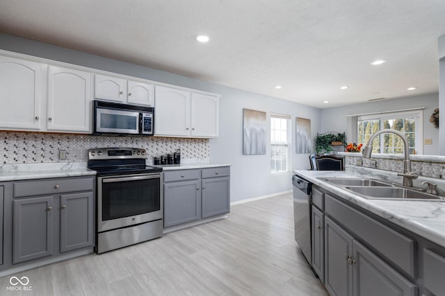 kitchen featuring stainless steel appliances, decorative backsplash, a sink, and gray cabinetry