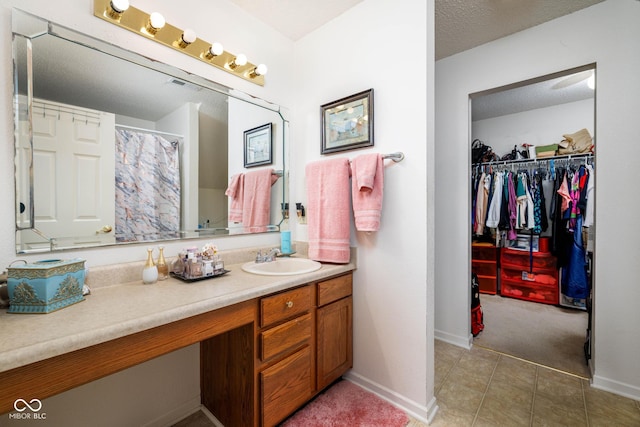 full bath with a textured ceiling, tile patterned flooring, vanity, baseboards, and a spacious closet