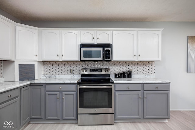 kitchen with light stone countertops, tasteful backsplash, appliances with stainless steel finishes, and gray cabinets