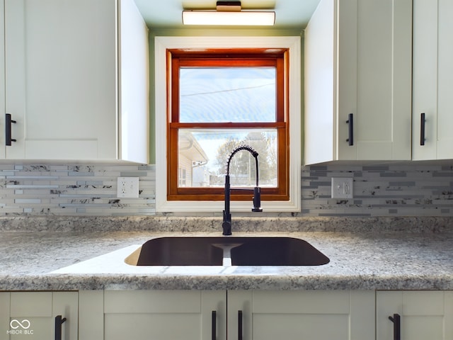 kitchen with white cabinets, a sink, and light stone countertops