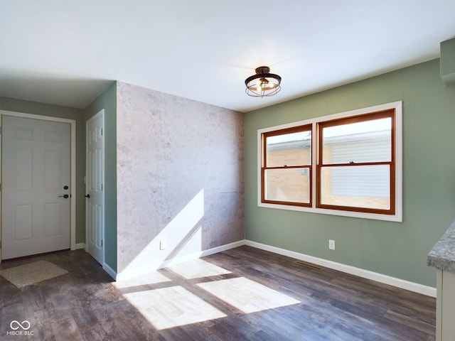 empty room with dark wood-style floors, visible vents, and baseboards