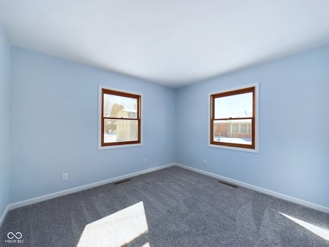 empty room featuring dark colored carpet, visible vents, and baseboards