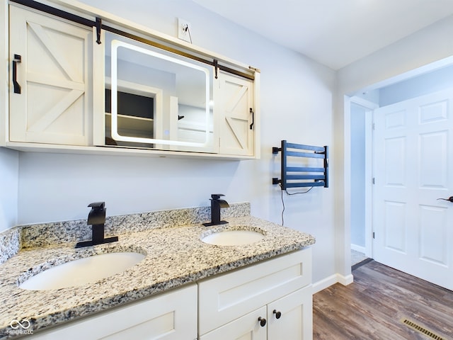 bathroom with double vanity, wood finished floors, a sink, and visible vents