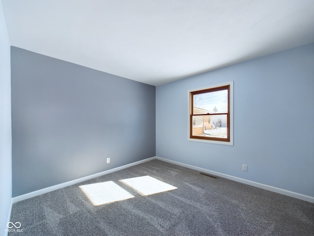 unfurnished room with baseboards, visible vents, and dark carpet