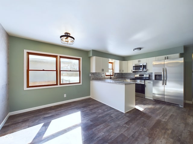 kitchen with white cabinets, appliances with stainless steel finishes, dark wood-style flooring, a peninsula, and a sink