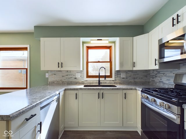 kitchen featuring a peninsula, a sink, white cabinetry, appliances with stainless steel finishes, and backsplash