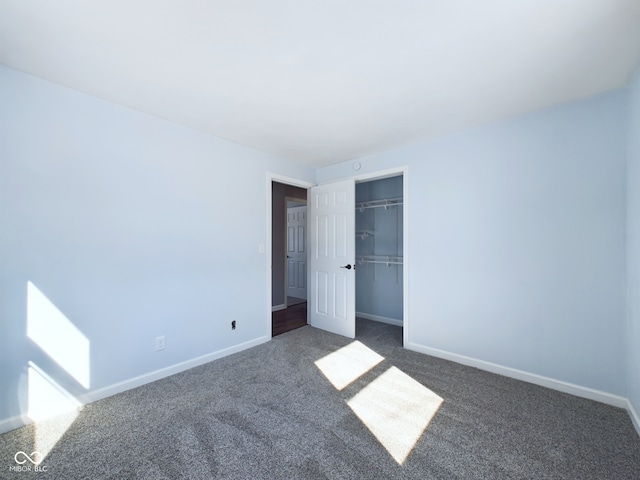 unfurnished bedroom with a closet, dark carpet, and baseboards