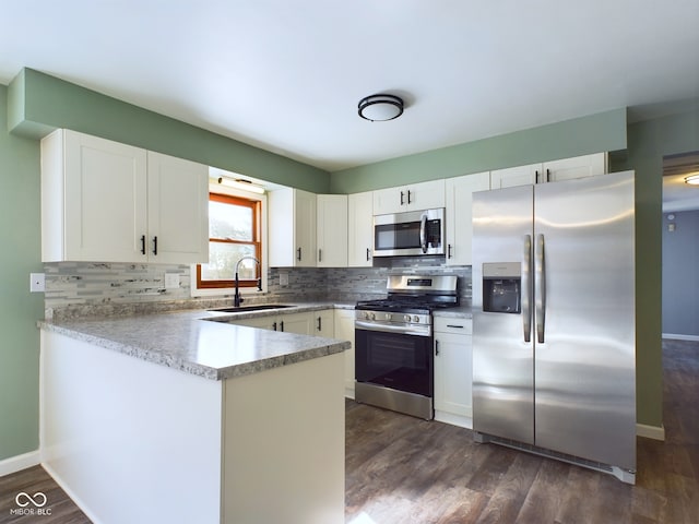 kitchen with tasteful backsplash, appliances with stainless steel finishes, white cabinets, a sink, and a peninsula