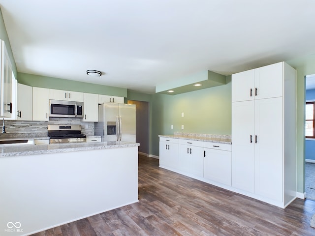 kitchen featuring white cabinets, dark wood finished floors, decorative backsplash, light stone counters, and stainless steel appliances