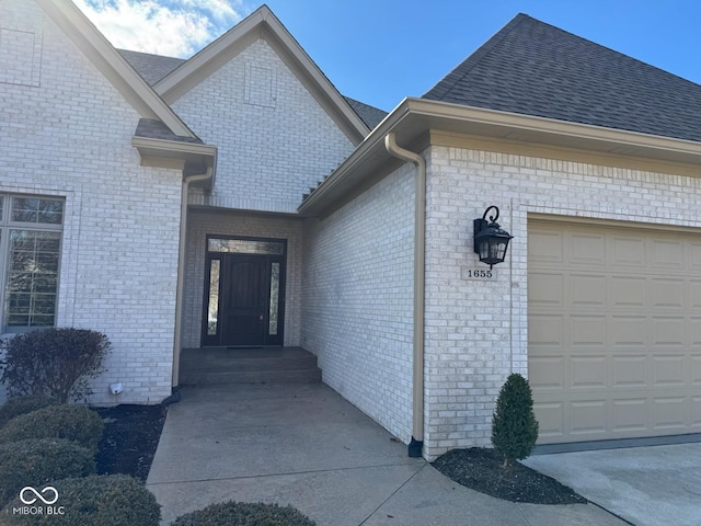 doorway to property with a garage and a shingled roof