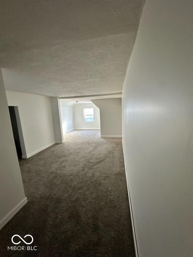 empty room featuring baseboards, dark colored carpet, and a textured ceiling