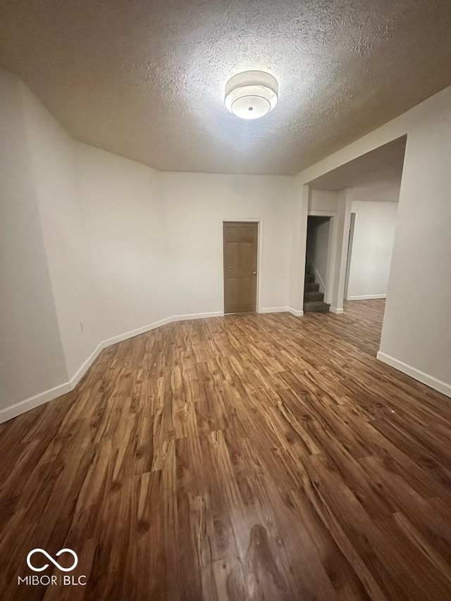 unfurnished room with a textured ceiling, wood finished floors, and baseboards