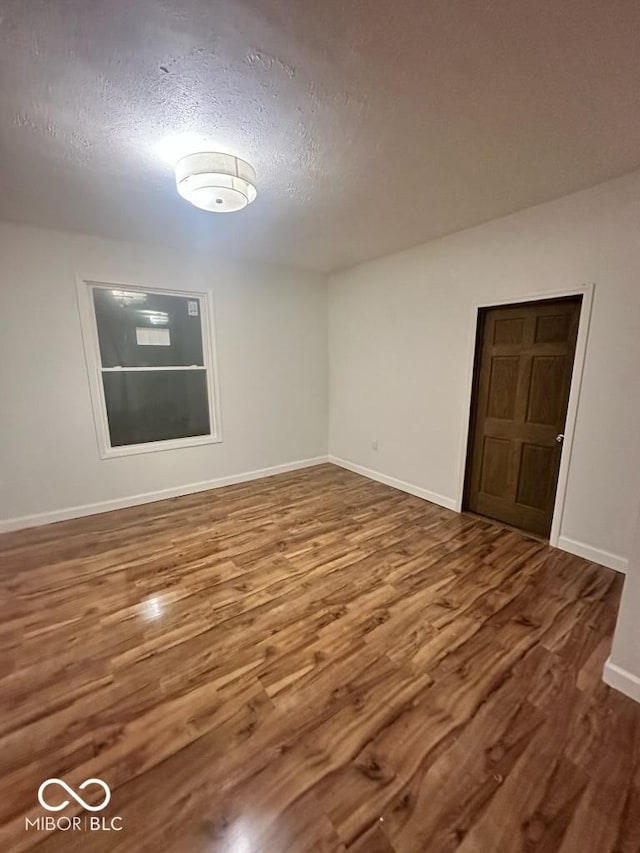 spare room with a textured ceiling, baseboards, and wood finished floors