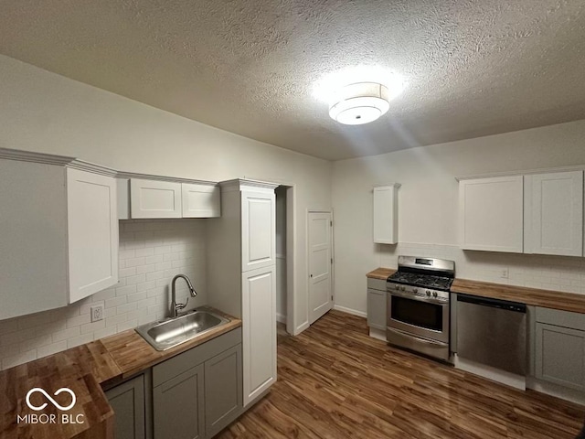 kitchen featuring appliances with stainless steel finishes, white cabinets, wooden counters, and a sink