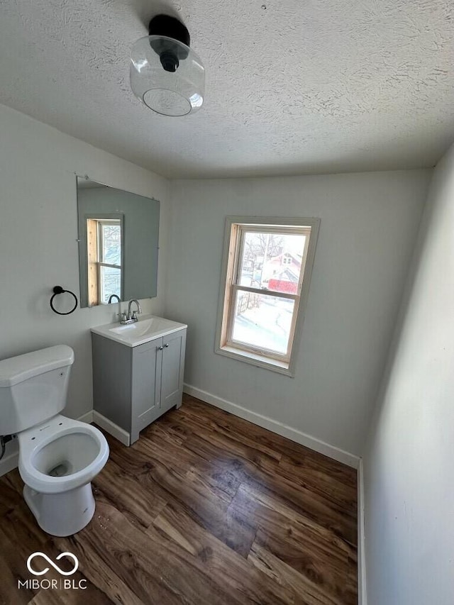 half bathroom with vanity, wood finished floors, toilet, and baseboards