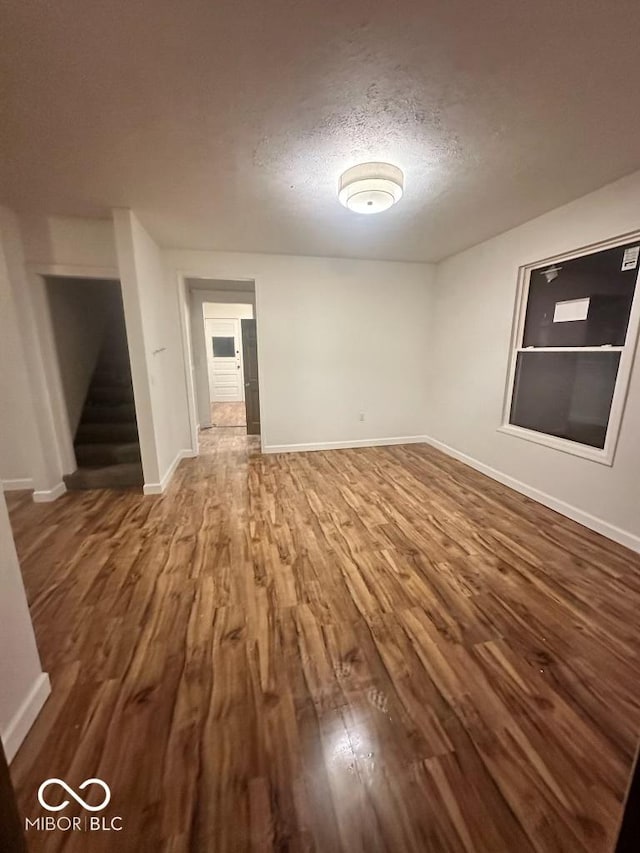 unfurnished living room with stairs, a textured ceiling, baseboards, and wood finished floors