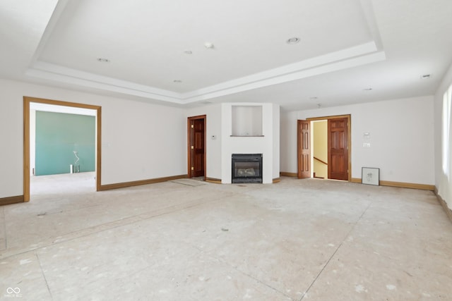 unfurnished living room with a glass covered fireplace, a tray ceiling, and baseboards